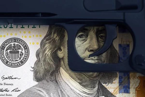 Auslöser der Waffe auf dem Hintergrund des auf die Banknoten gemalten Auges. Konzept des illegalen Waffenhandels. — Stockfoto