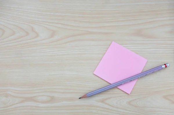 Blank pink paper with area for text or message, pencil and on wood table