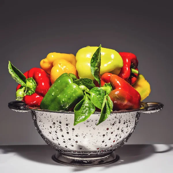 Fresh mixed colored bell peppers in a colander isolated on a dark. — Stock Photo, Image