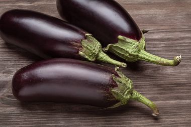 Ahşap bir yüzey üzerinde üç taze patlıcan.