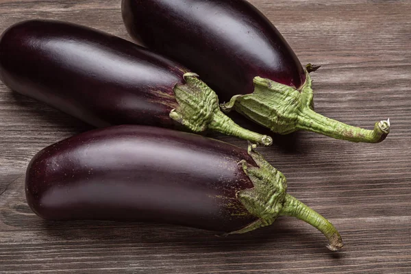 Ahşap bir yüzey üzerinde üç taze patlıcan.