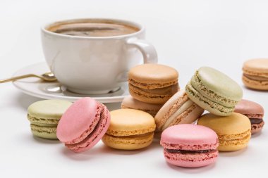 Çok renkli Fransızca macaroons, sıcak kahve. Beyaz Kupası ve fincan tabağı ve çay kaşığı beyaz arka plan üzerinde.