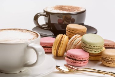 Siyah ve beyaz fincan cappuccino kahve, çay kaşığı ve renkli Fransızca macaroons.