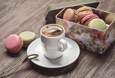Parlak metal kutu ve beyaz fincan kahve americano koyu ahşap yüzey üzerinde Fransızca macaroons.
