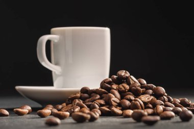 Büyük kahve çekirdekleri, beyaz fincan kahve koyu arka plan üzerine yığını. Kopya alanı.