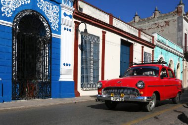 Camagüey, Cuba - 7 Mart 2018: Kırmızı klasik araba geçer bir mavi ve beyaz bina önünde