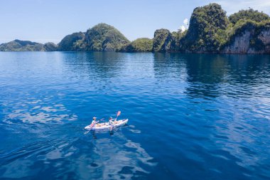 Kayakçılar mavi denizlerde gezerler ve Raja Ampat 'ın deniz manzarasından yükselen inanılmaz kireçtaşı adalarını keşfederler. Bu tropikal Endonezya bölgesi inanılmaz deniz biyolojik çeşitliliğiyle bilinir..