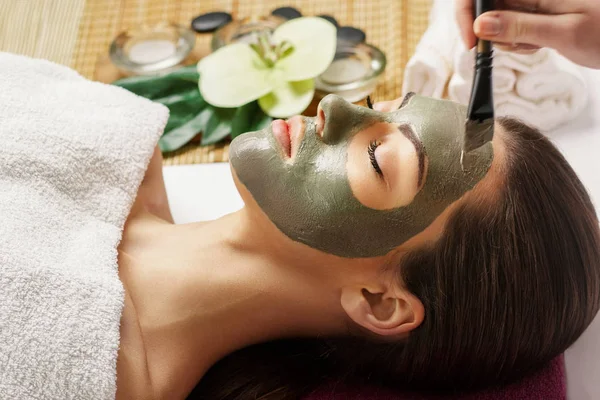 Face peeling mask, spa beauty treatment, skincare. Woman getting facial care by beautician at spa salon, side view, close-up.Spa clay mask on femele face.