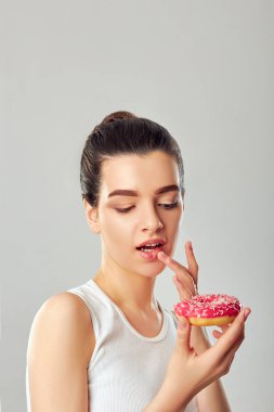 Güzellik mankeni kız pembe bir çörek tutuyor. Diyet olsun. Çok komik. Esmer kadın donut yiyor ve tadıyor. 