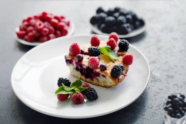 Bir parça yaban mersinli turta, ahududu ve beyaz tabakta tatlı olarak nane şekeri. Arka planda nefis ev yapımı kek parçaları