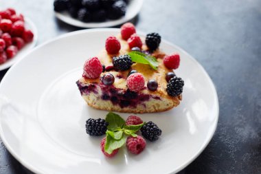 Bir parça yaban mersinli turta, ahududu ve beyaz tabakta tatlı olarak nane şekeri. Arka planda nefis ev yapımı kek parçaları