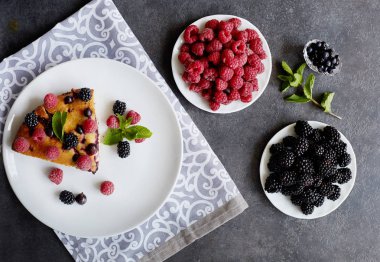 Bir parça yaban mersinli turta, ahududu ve beyaz tabakta tatlı olarak nane şekeri. Arka planda nefis ev yapımı kek parçaları
