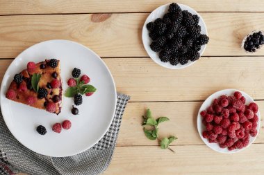 Beyaz bir tabakta yaban mersinli turta, ahududu ve nane şekeri, peçete. Tahta arka planda nefis ev yapımı kek parçaları.