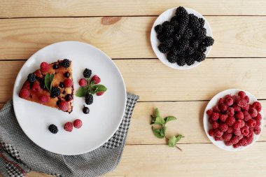 Beyaz bir tabakta yaban mersinli turta, ahududu ve nane şekeri, peçete. Tahta arka planda nefis ev yapımı kek parçaları.