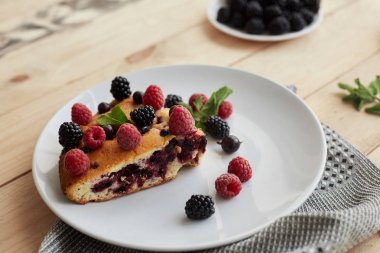 Beyaz bir tabakta yaban mersinli turta, ahududu ve nane şekeri, peçete. Tahta arka planda nefis ev yapımı kek parçaları.