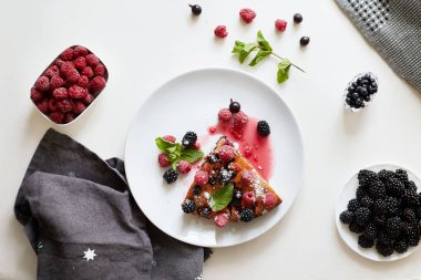 Bir parça yaban mersinli turta, ahududu ve beyaz tabakta tatlı olarak nane şekeri. Arka planda nefis ev yapımı kek parçaları