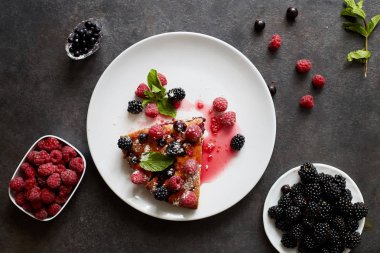 Bir parça yaban mersinli turta, ahududu ve beyaz tabakta tatlı olarak nane şekeri. Arka planda nefis ev yapımı kek parçaları