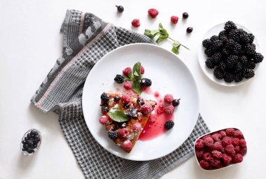 Bir parça yaban mersinli turta, ahududu ve beyaz tabakta tatlı olarak nane şekeri. Arka planda nefis ev yapımı kek parçaları