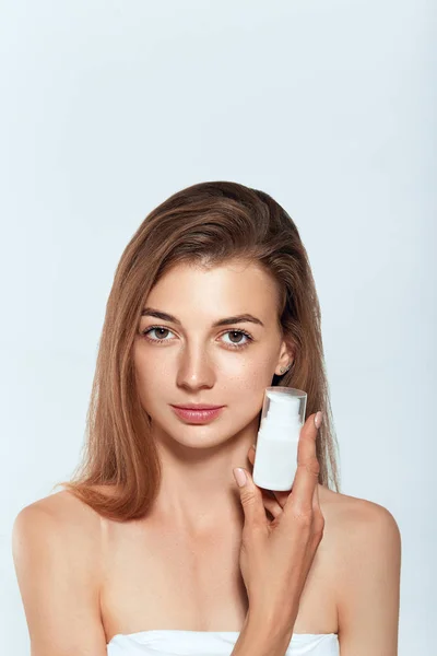 Beauty Face of Woman Concept. Skin care. Portrait of female model  holding and applying cosmetic moisturizing cream and touch own face. Skin Protection. Cosmetology. Spa