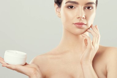 Kadın yüz cilt bakımı. Krem uygulamak ve şişe tutan çekici genç kadın portresi. Doğal makyaj ve taze cilt ile kız gülümseyerek, portre. Güzellik kozmetik. 