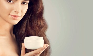 Cilt Bakımı. Güzellik kavramı. Kozmetik krem tutan genç güzel kadın. Yumuşak deri ve çıplak omuz, model makyajlı ışık çıplak, kadın tutarak onun elinde krem nemlendirici portresi. Cilt koruma ve Dermatoloji.