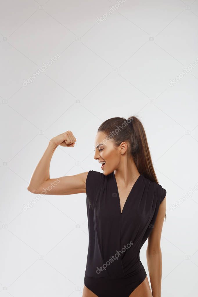 Portrait of a happy elegant woman showing her biceps on gray background