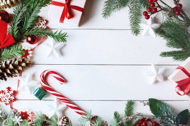 Beyaz arka planda Noel hediyesi kutuları, karlı köknar dalları, kozalaklı kozalaklar, bayram süslemeleri, karamel çubukları ve kırmızı böğürtlenli güzel bir Noel kompozisyonu. Üst görünüm, alanı kopyala.