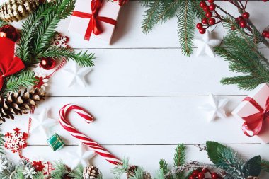 Beyaz arka planda Noel hediyesi kutuları, karlı köknar dalları, kozalaklı kozalaklar, bayram süslemeleri, karamel çubukları ve kırmızı böğürtlenli güzel bir Noel kompozisyonu. Üst görünüm, alanı kopyala.