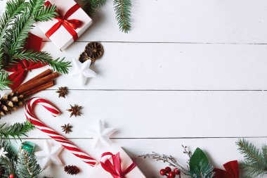 Beyaz arka planda Noel hediyesi kutuları, karlı köknar dalları, kozalaklı kozalaklar, bayram süslemeleri, karamel çubukları ve kırmızı böğürtlenli güzel bir Noel kompozisyonu. Üst görünüm, alanı kopyala.