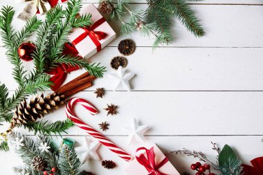 Altın Noel hediye kutuları, karlı köknar dalları, kozalaklı kozalaklar, bayram süslemeleri ve kırmızı böğürtlenli beyaz arka planda güzel bir Noel kompozisyonu. Üst görünüm