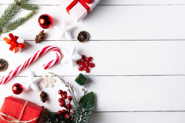 Noel hediyesi kutuları, karlı köknar dalları, kozalaklı kozalaklar, tarçınlı kurutulmuş meyveler, bayram süslemeleri, karamel çubukları olan ahşap beyaz arka planda güzel bir Noel kompozisyonu. Yeni yıl. Üst görünüm, alanı kopyala.