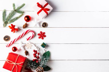 Noel hediyesi kutuları, karlı köknar dalları, kozalaklı kozalaklar, tarçınlı kurutulmuş meyveler, bayram süslemeleri, karamel çubukları olan ahşap beyaz arka planda güzel bir Noel kompozisyonu. Yeni yıl. Üst görünüm, alanı kopyala.