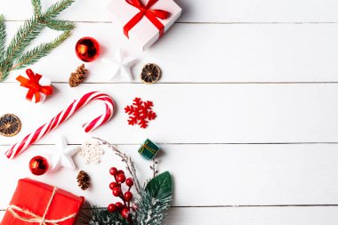 Noel hediyesi kutuları, karlı köknar dalları, kozalaklı kozalaklar, tarçınlı kurutulmuş meyveler, bayram süslemeleri, karamel çubukları olan ahşap beyaz arka planda güzel bir Noel kompozisyonu. Yeni yıl. Üst görünüm, alanı kopyala.