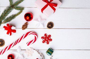 Noel hediyesi kutuları, karlı köknar dalları, kozalaklı kozalaklar, tarçınlı kurutulmuş meyveler, bayram süslemeleri, karamel çubukları olan ahşap beyaz arka planda güzel bir Noel kompozisyonu. Yeni yıl. Üst görünüm, alanı kopyala.