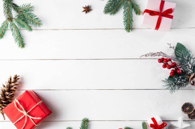 Noel hediyesi kutuları, karlı köknar dalları, kozalaklı kozalaklar, tarçınlı kurutulmuş meyveler, bayram süslemeleri, karamel çubukları olan ahşap beyaz arka planda güzel bir Noel kompozisyonu. Yeni yıl. Üst görünüm, alanı kopyala.