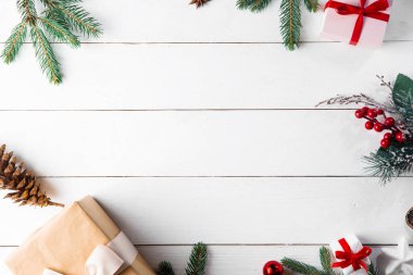 Noel hediyesi kutuları, karlı köknar dalları, kozalaklı kozalaklar, tarçınlı kurutulmuş meyveler, bayram süslemeleri, karamel çubukları olan ahşap beyaz arka planda güzel bir Noel kompozisyonu. Yeni yıl. Üst görünüm, alanı kopyala.