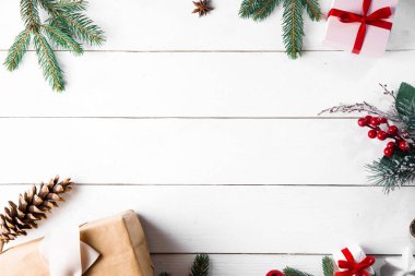 Noel hediyesi kutuları, karlı köknar dalları, kozalaklı kozalaklar, tarçınlı kurutulmuş meyveler, bayram süslemeleri, karamel çubukları olan ahşap beyaz arka planda güzel bir Noel kompozisyonu. Yeni yıl. Üst görünüm, alanı kopyala.