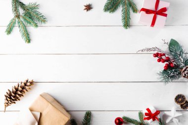 Noel hediyesi kutuları, karlı köknar dalları, kozalaklı kozalaklar, tarçınlı kurutulmuş meyveler, bayram süslemeleri, karamel çubukları olan ahşap beyaz arka planda güzel bir Noel kompozisyonu. Yeni yıl. Üst görünüm, alanı kopyala.