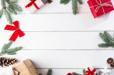 Noel hediyesi kutuları, karlı köknar dalları, kozalaklı kozalaklar, tarçınlı kurutulmuş meyveler, bayram süslemeleri, karamel çubukları olan ahşap beyaz arka planda güzel bir Noel kompozisyonu. Yeni yıl. Üst görünüm, alanı kopyala.