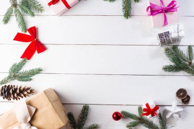 Noel hediyesi kutuları, karlı köknar dalları, kozalaklı kozalaklar, tarçınlı kurutulmuş meyveler, bayram süslemeleri, karamel çubukları olan ahşap beyaz arka planda güzel bir Noel kompozisyonu. Yeni yıl. Üst görünüm, alanı kopyala.