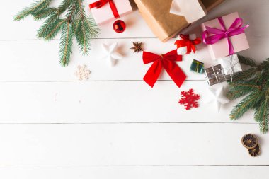 Noel hediyesi kutuları, karlı köknar dalları, kozalaklı kozalaklar, tarçınlı kurutulmuş meyveler, bayram süslemeleri, karamel çubukları olan ahşap beyaz arka planda güzel bir Noel kompozisyonu. Yeni yıl. Üst görünüm, alanı kopyala.