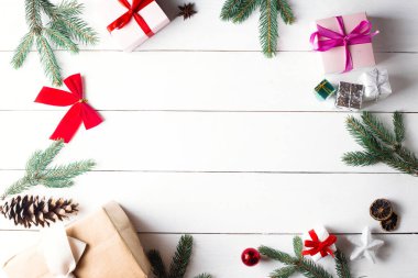 Noel hediyesi kutuları, karlı köknar dalları, kozalaklı kozalaklar, tarçınlı kurutulmuş meyveler, bayram süslemeleri, karamel çubukları olan ahşap beyaz arka planda güzel bir Noel kompozisyonu. Yeni yıl. Üst görünüm, alanı kopyala.