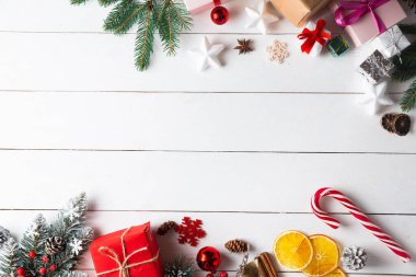 Noel hediyesi kutuları, karlı köknar dalları, kozalaklı kozalaklar, tarçınlı kurutulmuş meyveler, bayram süslemeleri, karamel çubukları olan ahşap beyaz arka planda güzel bir Noel kompozisyonu. Yeni yıl. Üst görünüm, alanı kopyala.