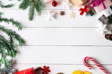 Noel hediyesi kutuları, karlı köknar dalları, kozalaklı kozalaklar, tarçınlı kurutulmuş meyveler, bayram süslemeleri, karamel çubukları olan ahşap beyaz arka planda güzel bir Noel kompozisyonu. Yeni yıl. Üst görünüm, alanı kopyala.