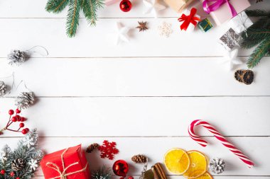 Noel hediyesi kutuları, karlı köknar dalları, kozalaklı kozalaklar, tarçınlı kurutulmuş meyveler, bayram süslemeleri, karamel çubukları olan ahşap beyaz arka planda güzel bir Noel kompozisyonu. Yeni yıl. Üst görünüm, alanı kopyala.