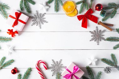 Noel hediyesi kutuları, karlı köknar dalları, kozalaklı kozalaklar, tarçınlı kurutulmuş meyveler, bayram süslemeleri, karamel çubukları olan ahşap beyaz arka planda güzel bir Noel kompozisyonu. Yeni yıl. Üst görünüm, alanı kopyala.