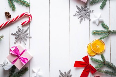 Noel hediyesi kutuları, karlı köknar dalları, kozalaklı kozalaklar, tarçınlı kurutulmuş meyveler, bayram süslemeleri, karamel çubukları olan ahşap beyaz arka planda güzel bir Noel kompozisyonu. Yeni yıl. Üst görünüm, alanı kopyala.