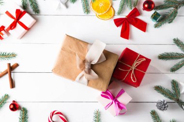 Noel hediyesi kutuları, karlı köknar dalları, kozalaklı kozalaklar, tarçınlı kurutulmuş meyveler, bayram süslemeleri, karamel çubukları olan ahşap beyaz arka planda güzel bir Noel kompozisyonu. Yeni yıl. Üst görünüm, alanı kopyala.