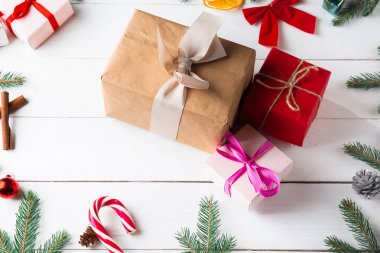 Noel hediyesi kutuları, karlı köknar dalları, kozalaklı kozalaklar, tarçınlı kurutulmuş meyveler, bayram süslemeleri, karamel çubukları olan ahşap beyaz arka planda güzel bir Noel kompozisyonu. Yeni yıl. Üst görünüm, alanı kopyala.