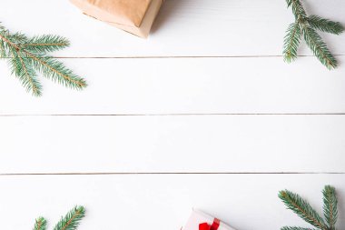 Noel hediyesi kutuları, karlı köknar dalları, kozalaklı kozalaklar, tarçınlı kurutulmuş meyveler, bayram süslemeleri, karamel çubukları olan ahşap beyaz arka planda güzel bir Noel kompozisyonu. Yeni yıl. Üst görünüm, alanı kopyala.